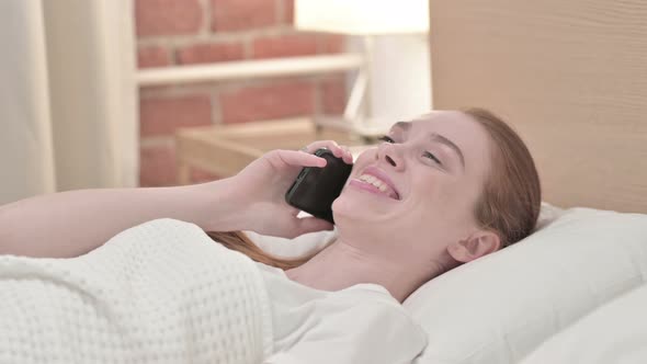 Redhead Young Woman Talking on Smartphone in Bed 