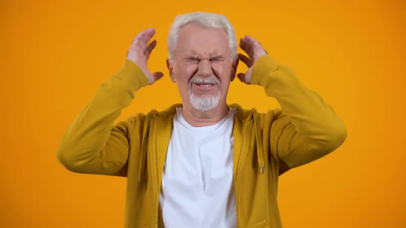 Elderly Man Closing Ears by Palms, Irritated With Gossips, Orange Background