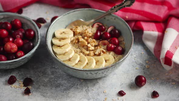 Ceramic Bowl of Oatmeal Porridge with Banana, Fresh Cranberries and Walnuts