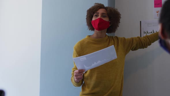 Mixed race woman wearing face mask in office giving presentation