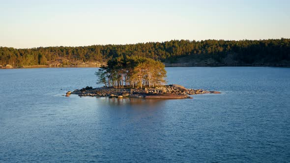 Small Island In Light Of Sunset In Sea Near The Shore With A Coniferous Forest