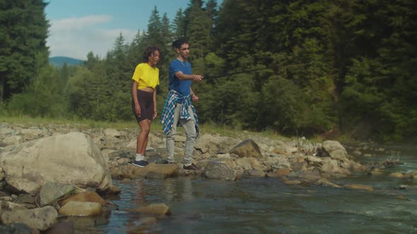 Positive Arab Man Teaching Lovely African American Woman to Fish on Mountain River