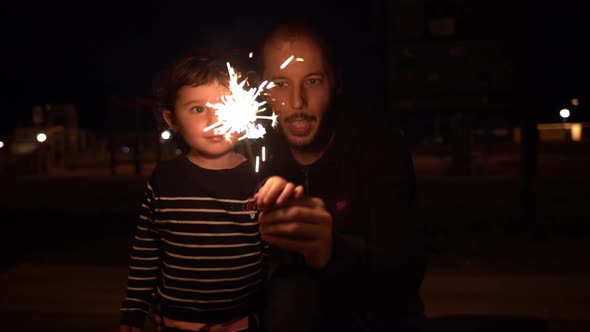 Little girl and father holding sparkler at night
