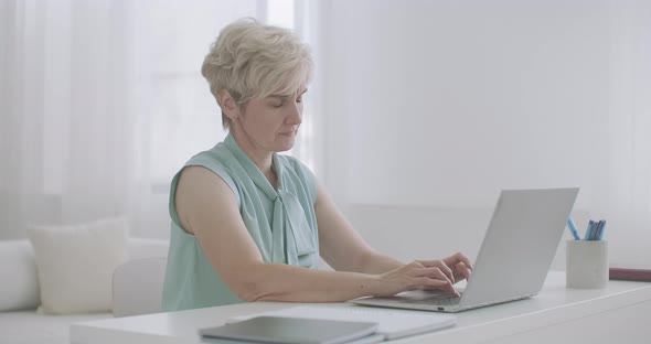 Middle-aged Woman with Headache Is Working with Laptop in Home, Touching Forehead By Hands, Tired