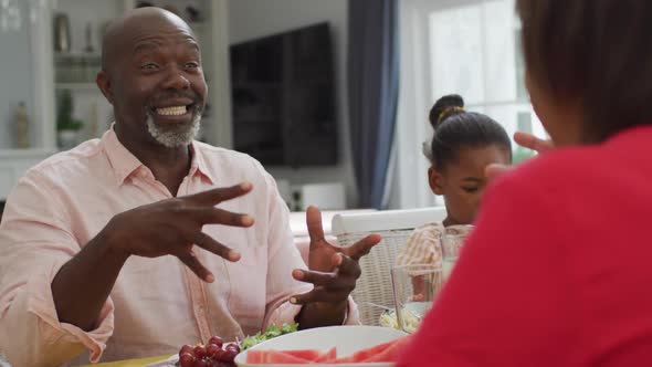 Happy african american grandfather talking, eating lunch with family at home