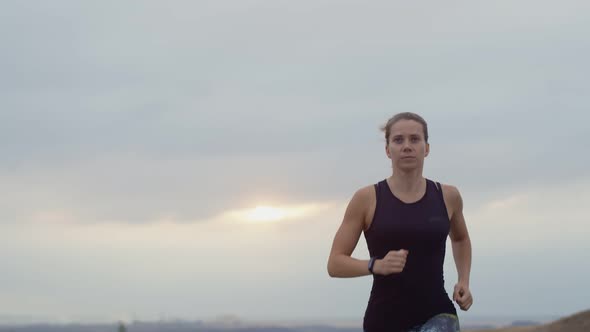 Caucasian Woman is Running Intently Outdoors Against Background of Overcast Clouds Doing Daily