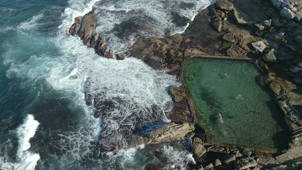Ocean waves crashing on the rocks. People swimming in a rockpool by the rocky beach at Maroubra, Syd