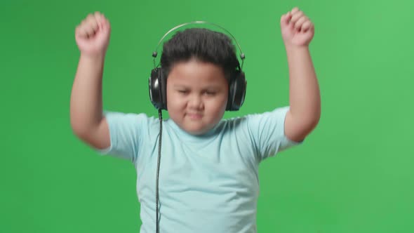 Asian Little Boy Listening To Music With Headphones And Dancing In The Green Screen Studio