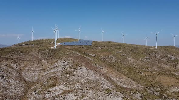 Aerial panoramic shot of turbine farm and solar panels on green mountain during sunlight
