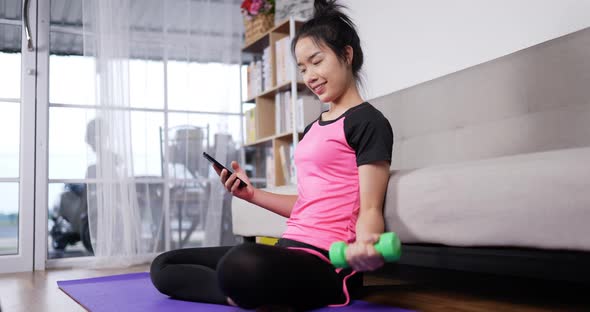 Woman holding smartphone and training dumbbells