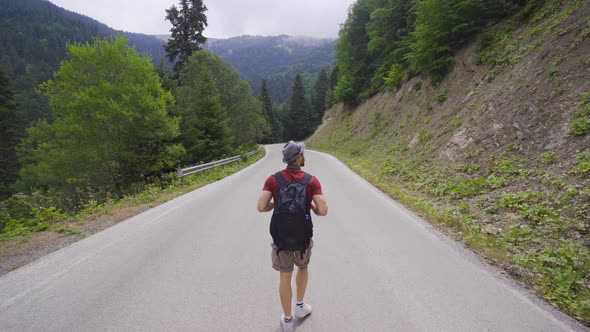 Man walking on asphalt road in forest.