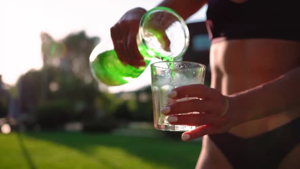 Slim Woman in Swimsuit Pours Refreshing Drink Pieces Ice From Bottle Into Glass