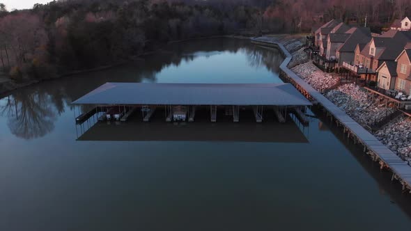 Aerial drone footage flying over calm water and boat docks with nice houses on the right at sunset