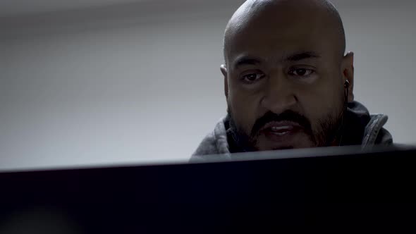 A bald and handsome Asian man looking stern while conversing with someone on the laptop screen.