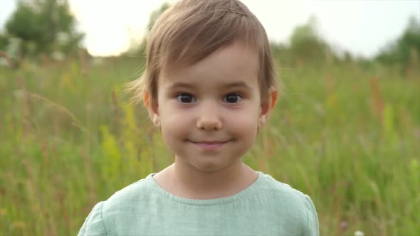 a Little Girl on the Wild Field Looks Into the Camera Lens and Smiles