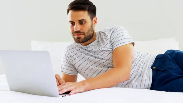 Man using laptop on bed in bedroom