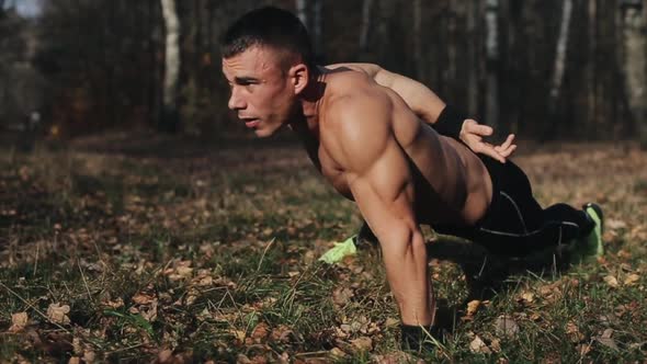 Young Muscular Athletic Man Exercising Doing Push-ups on One Arm in the Forest. Strong Caucasian Guy