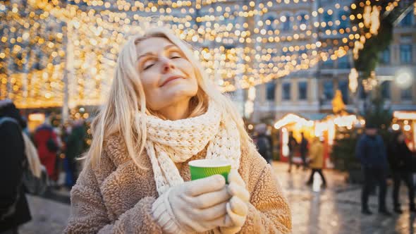 Portrait of Beautiful Senior Lady Warming Hands with Takeaway Coffee Standing at Decorated City