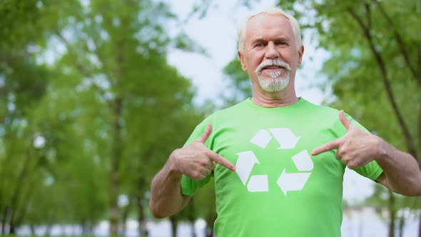 Smiling Mature Male Pointing at Recycling Symbol on Green T-Shirt Ecology