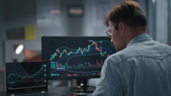 Rear View of Trader Working with Stock Market on Laptop Late in Office