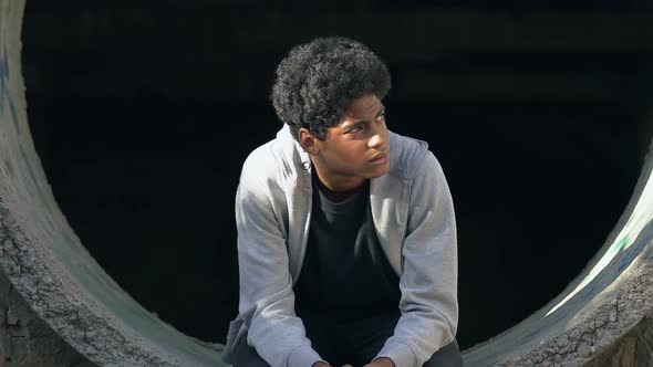 Upset mixed-race teen boy sitting alone in abandoned lane