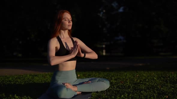 Attractive young woman is meditating sitting in lotus position sitting on yoga mat with closed eyes.