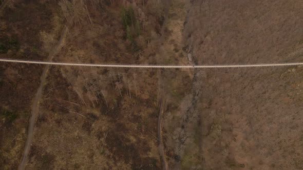Aerial high angle reveal shot of a tourist crossing Germany's longest suspension bridge on a dry win