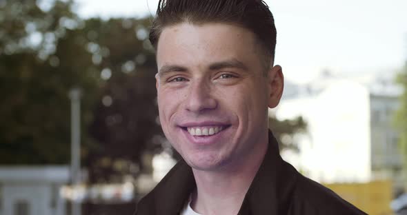 Handsome Brunette Guy with Freckles on Male Face Looks at Camera Posing Stands Outdoors Smiling Wide