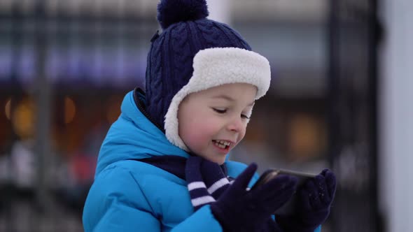 Little Boy in Winter Wear Using Phone on Cold Snowy Day