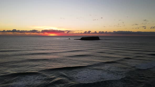 Moving drone view travelling over breaking waves with a silhouette of a Marine Park Island and color