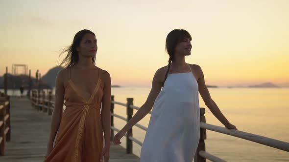 Two Young Woman Models are Walking in the Evening Pier During Sun Set Time Evening Dress