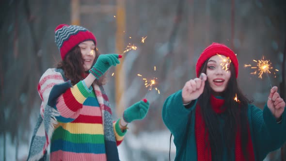 Two Young Happy Women Standing Outdoors with Lighted Up Sparklers