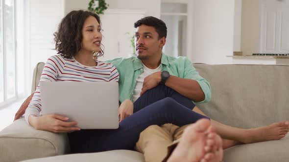 Hispanic couple sitting on sofa looking at laptop discussing