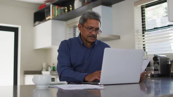 Senior mixed race man using laptop in kitchen