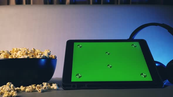 Tablet computer with green touch screen and popcorn in a big bowl on sofa.