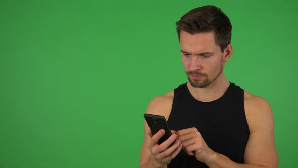 A Young Handsome Athlete Works on a Smartphone - Green Screen Studio