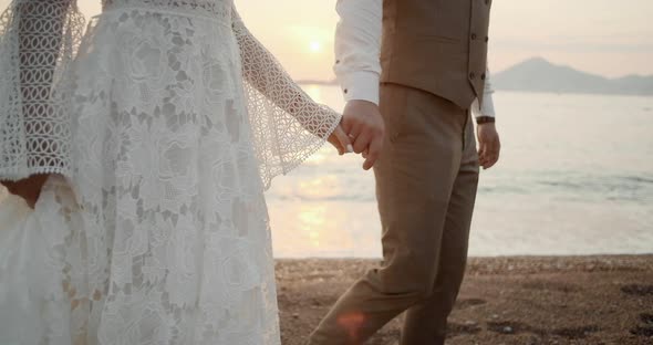 Hands of the bride and groom walking along the beach at sunset