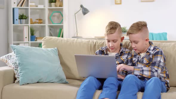 10-Year-Old Boy Doing Homework on Laptop and Twin Interfering alt