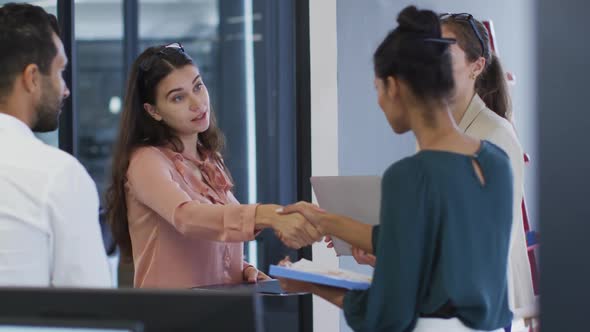 Two diverse businesswomen standing shaking hands during meeting with colleagues