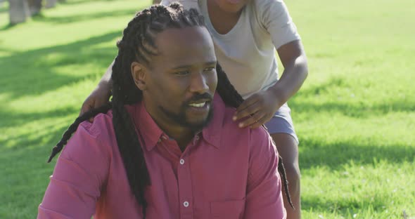 Video of happy african american father and son having picnic on grass and hugging