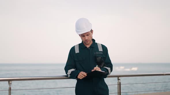 Port Inspector Standing at Dockside in Port and Writing Report During Marine Ship Vessel Inspection