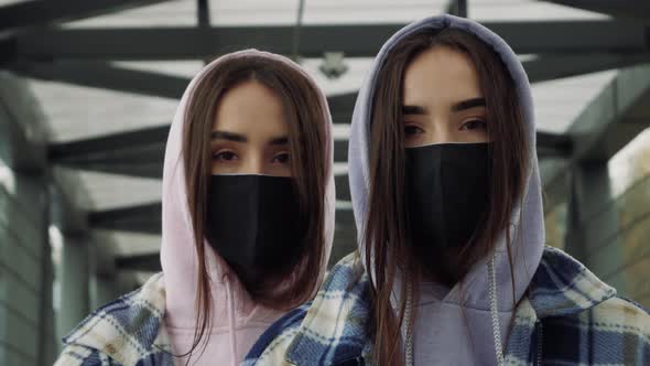 Portrait of a beautiful young twins girls wearing protective face mask standing close and looking on