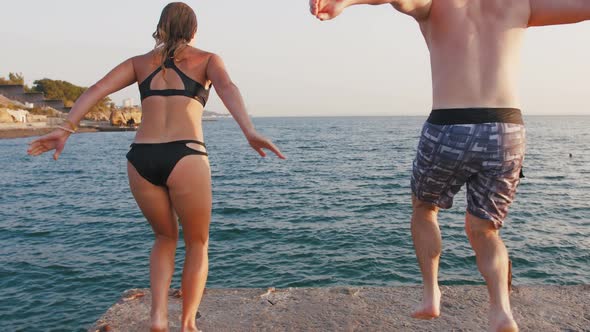 Young Woman and Man Jumping From a Pier Into the Sea and Doing Tricks During Beautiful Sunrise Slow