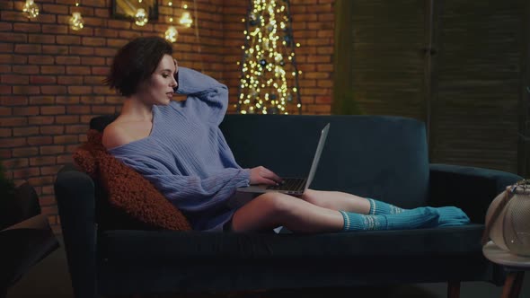 Pretty Girl Relaxing on Sofa in Cozy Room and Uses Laptop