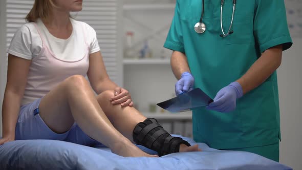 Professional Surgeon Talking About Broken Bone X-Ray to Female in Ankle Wrap