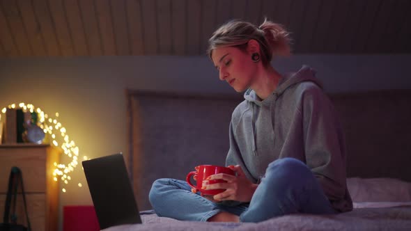 Pensive woman watching something on laptop with cup of tea