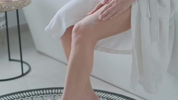 Close up female legs, woman applying  oil lotion on her body in bathroom.