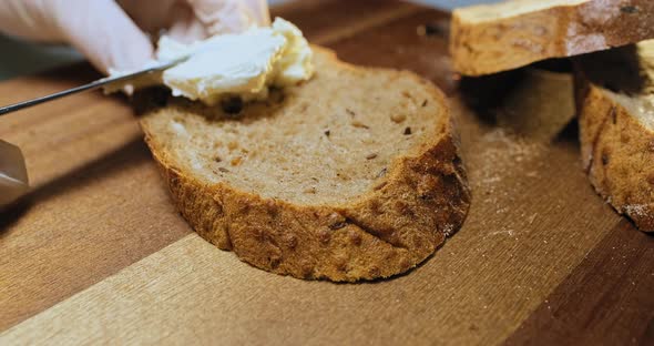 Person Spreads Cream Cheese on Rye Bread Slice on Table