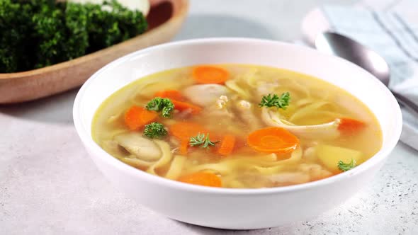 Homemade chicken soup with noodles and vegetables in white bowl, white background. 