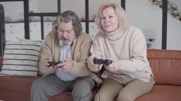 Cheerful Absorbed Senior Man and Woman Playing Video Games with Game Consoles, Portrait of Joyful